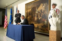 Barack Obama seating at a desk, signing a book. Standing at left Gérard Araud.
