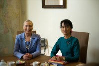 Hilary Clinton and Aung San Suu Kyi seating next to each other, hands crossed, smiling.