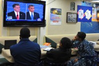 Three people seating in front of a TV, watching Obama and Mitt Romney debating.