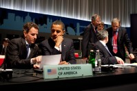 Barack Obama seating with Timothy Geithner, looking at the paper that he is showing him. In the first plan, "United States of America" sign.