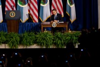 Obama on stage, signing a document. In the background, American and Tribal flags.