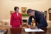 Elena Kagan watching Barack Obama sign a paper. 