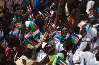 A crowd celebrating, waving south sudanese flags.