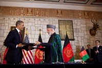 Barack Obama and Hamid Karzai exchange documents. In the background, US and Afghan flags.