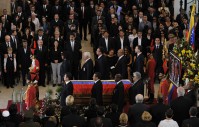 A crowd standing, surrounding a casket.